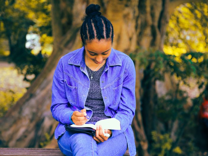 selective focus photography of woman reading book while sitting at bench