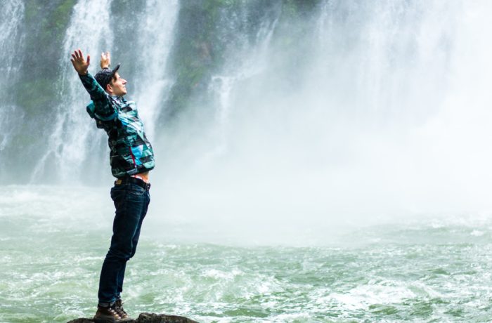 man standing on black rock surrounded body of water