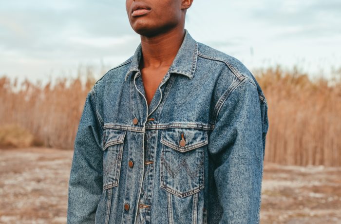 man in blue denim jacket standing on brown field during daytime