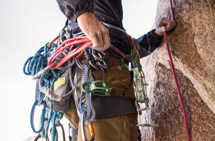 rock climber holding red rope strapped on waist while on side of brown boulder at daytime
