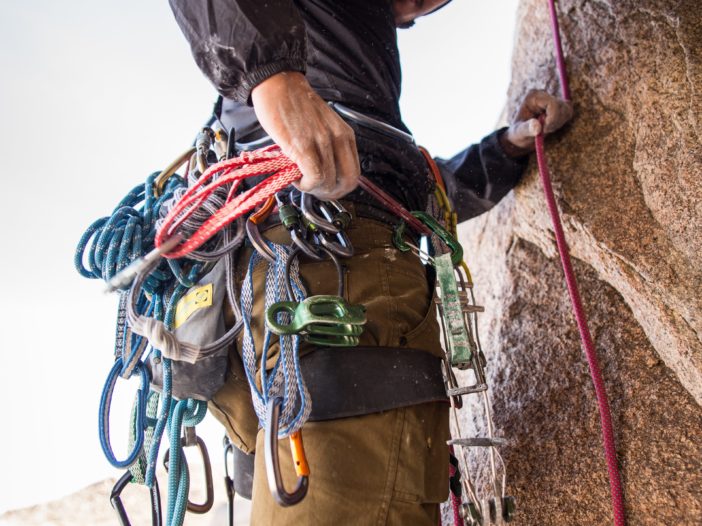 rock climber holding red rope strapped on waist while on side of brown boulder at daytime