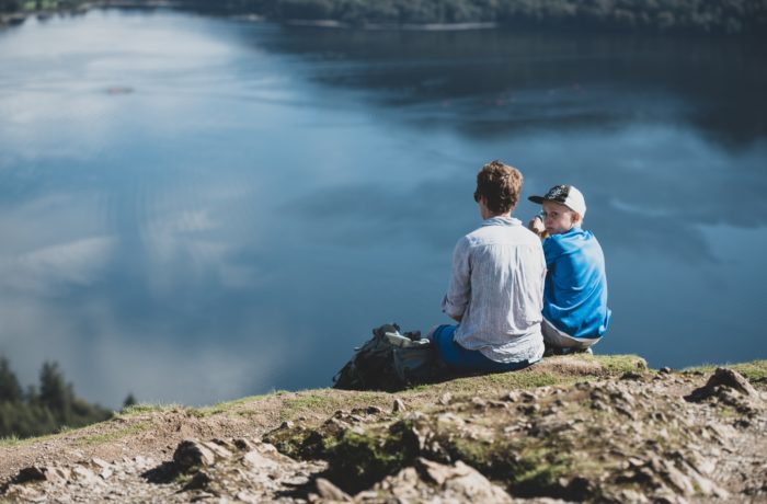 man sitting on field beside body of water