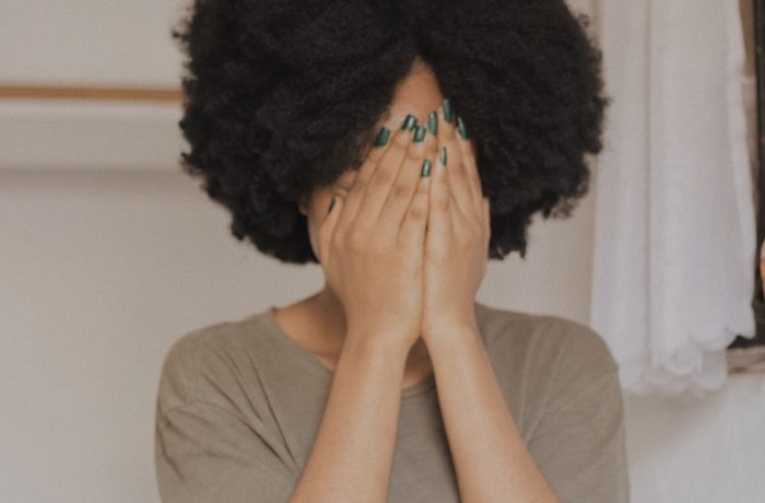 woman in gray t-shirt covering face with both hands