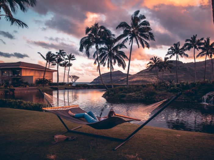 person on brown hammock with steel base across body of water